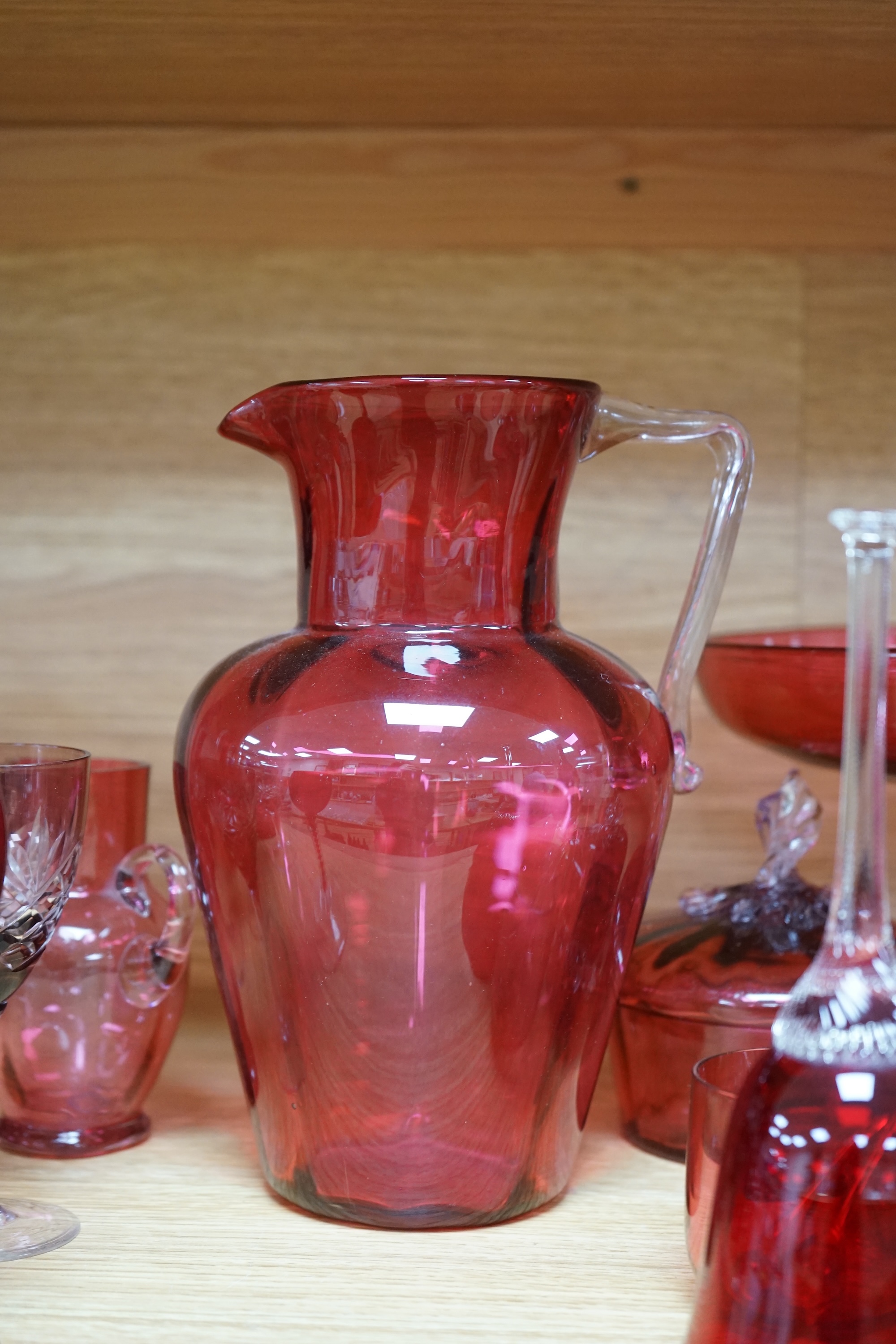 Mixed cranberry glassware to include jugs, glasses, jars and a comport, largest 23cm high. Condition - fair to good